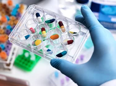 De foto toont een hand met blauwe handschoen, die een bakje met medicijnen vasthoudt