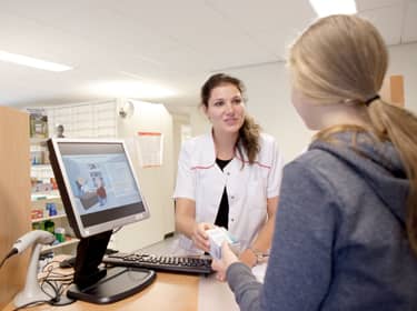 De foto toont een apotheker die medicijnen overhandigt aan een patiënt