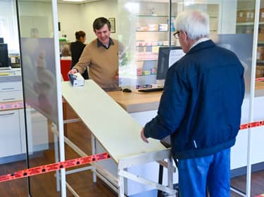 De foto toont een apotheekmedewerker die op anderhalve meter afstand een medicijn afgeeft aan een man