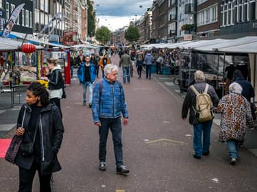De foto toont een marktplein met wandelende mensen