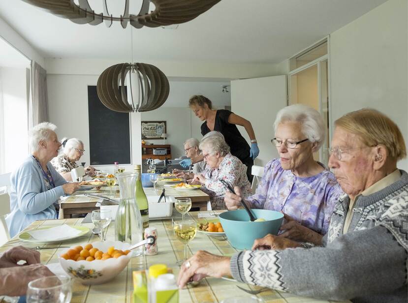 De foto toont een groep ouderen die aan het eten zijn in een verpleeghuis.