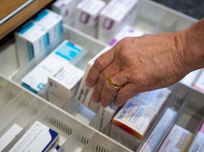 Op de foto staat een hand die medicijnen uit een lade pakt.