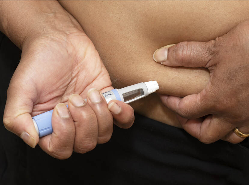 De foto toont een close-up van een hand van iemand die zichzelf in een buikplooi injecteert met een medicijn